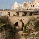 Il viottolo a un certo punto va in salita e ci porta in un punto in cui, girandoci, possiamo avere una visione d�insieme dei due ponti con alle spalle le case del centro storico di Polignano a picco sul mare